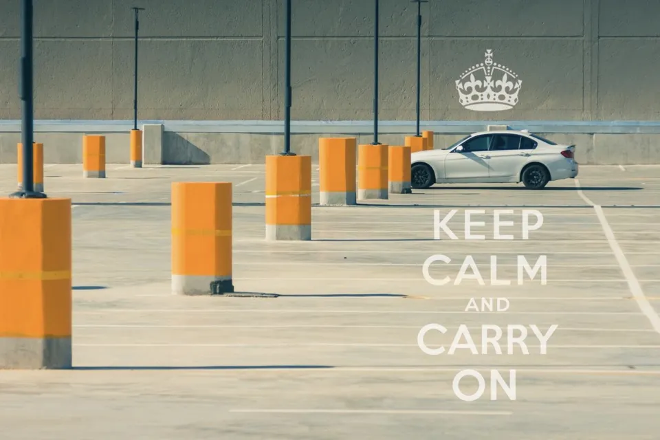 A single car in an empty parking lot full of only bright yellow bollards. A caption on the image reads, "Keep calm and carry on."